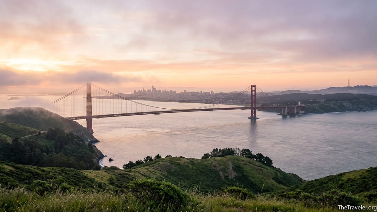Golden Gate Bridge at sunrise with San Francisco skyline and misty hills beyond.