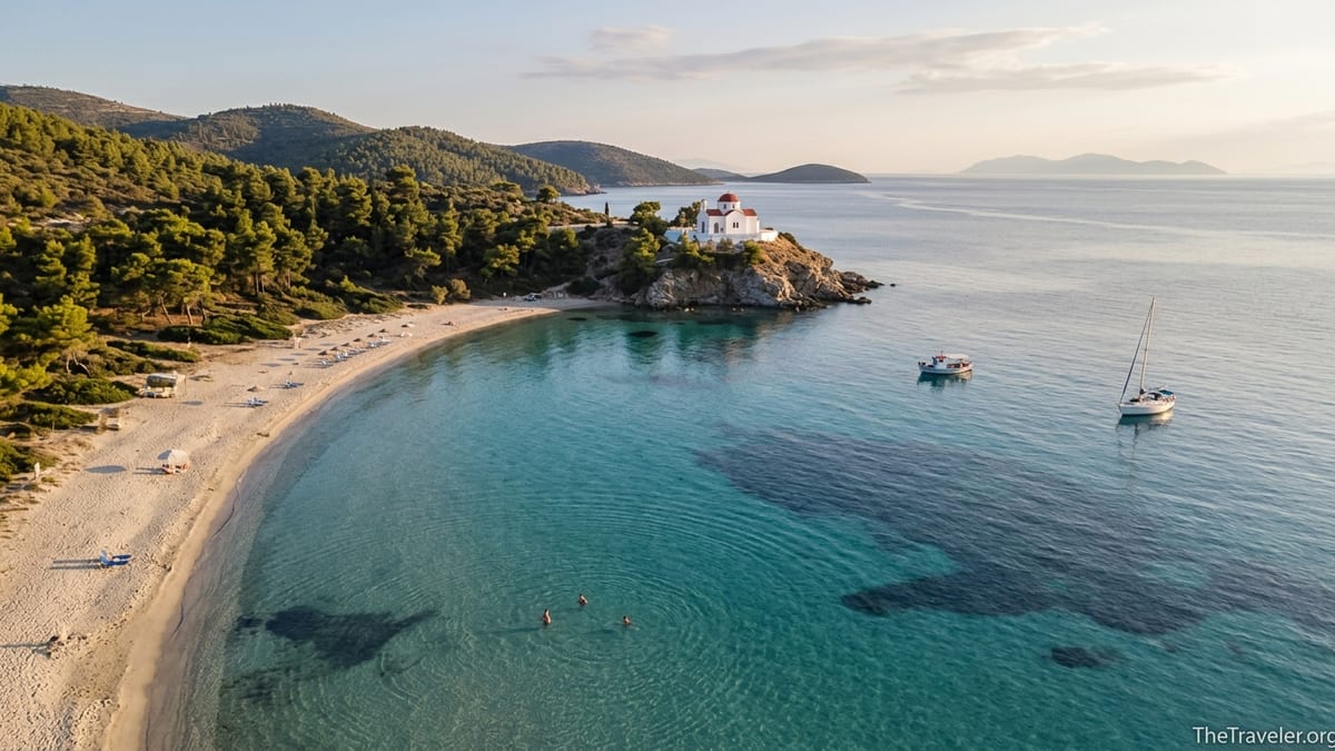 Quiet sandy bay in the Dodecanese with turquoise water, pine-clad hills and a few well spaced sunbeds.