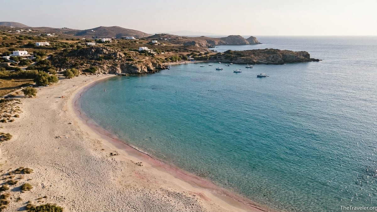 Aerial view of a sandy Greek island beach with turquoise water and rocky headlands at sunset.