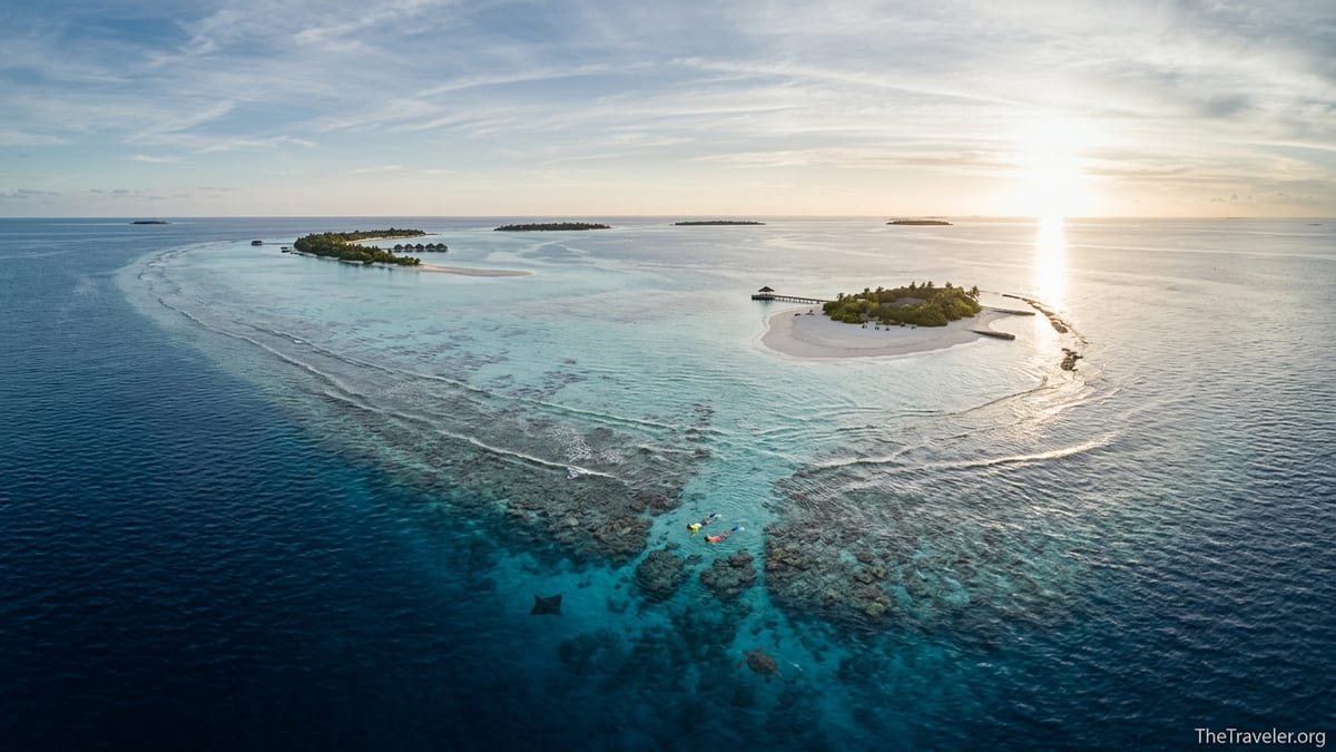Aerial view of a Maldivian atoll with reef edge, lagoon and snorkelers in clear water.