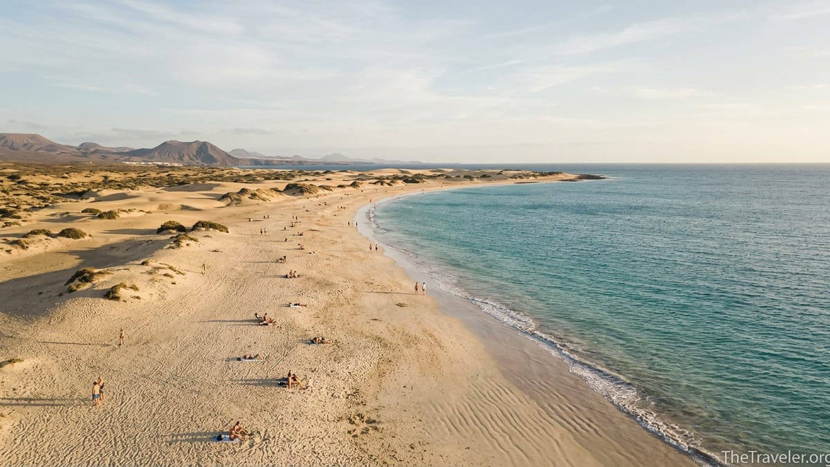 Golden Canary Islands beach with dunes and turquoise sea at sunset, viewed from above.