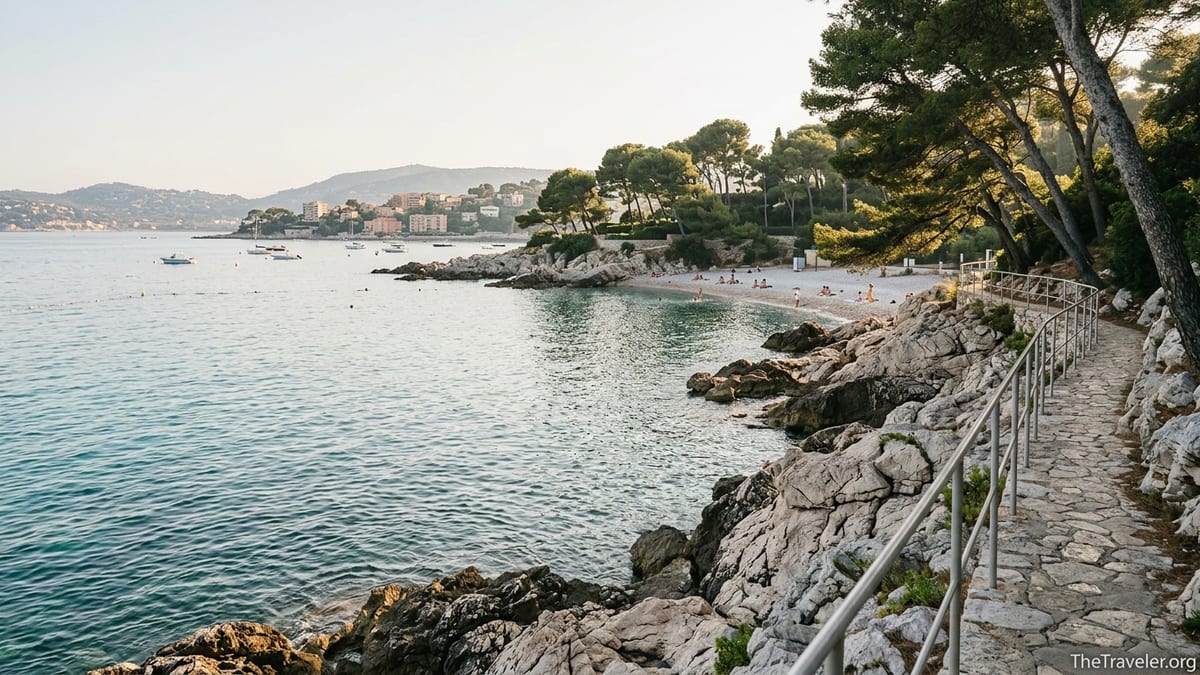 Coastal path above a turquoise cove on Cap Ferrat with pines, cliffs, and a small beach.