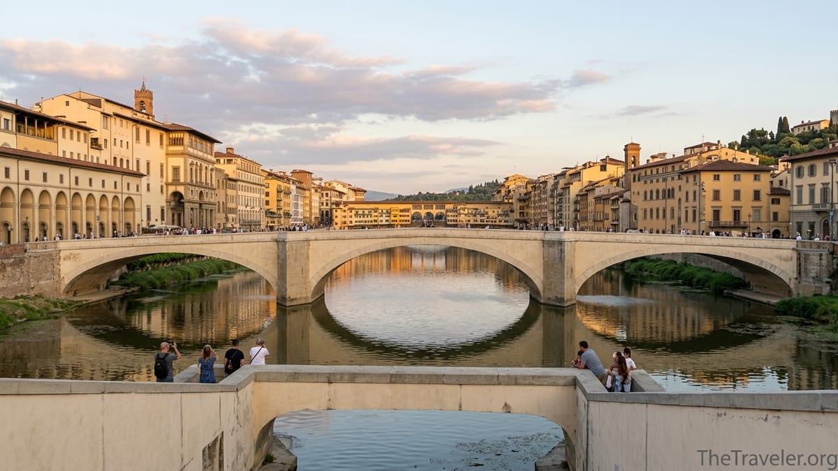 View from Ponte alle Grazie over the Arno toward Ponte Vecchio at sunset with a few visitors on the bridge.