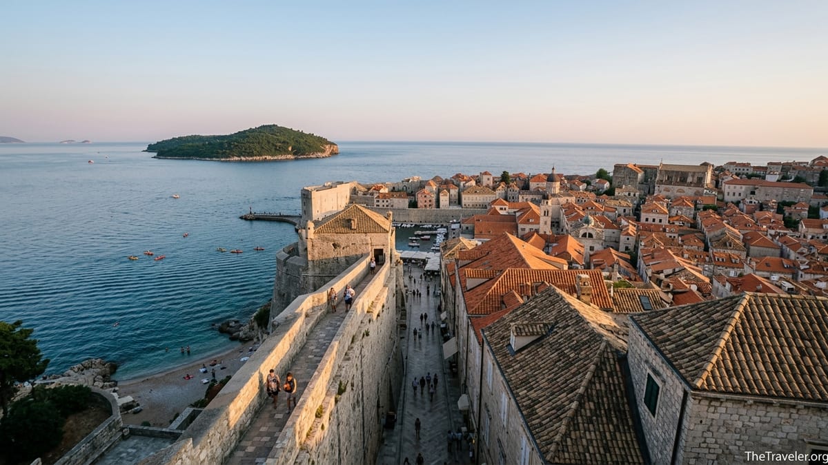 View from Dubrovnik city walls over Old Town rooftops toward Lokrum Island at sunset.