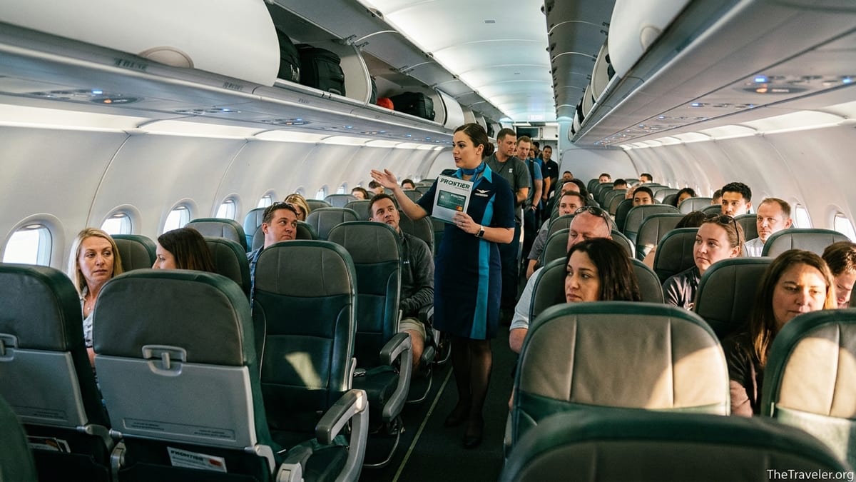 Frontier Airlines flight attendant holding a credit card brochure in a crowded budget airline cabin