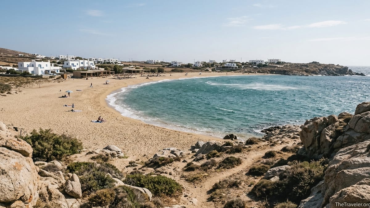 Windy Ftelia Beach bay in Mykonos with open sand and turquoise waves seen from a rocky headland.