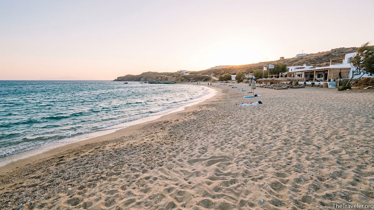 Windy morning view of Ftelia Beach in Mykonos with waves, open sand and a distant boho beach club.