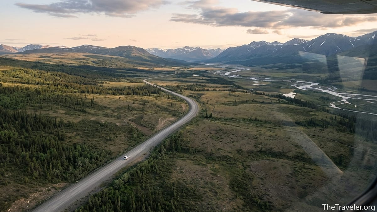 Aerial view of a gravel highway crossing tundra and low mountains in northern Canada at sunset.