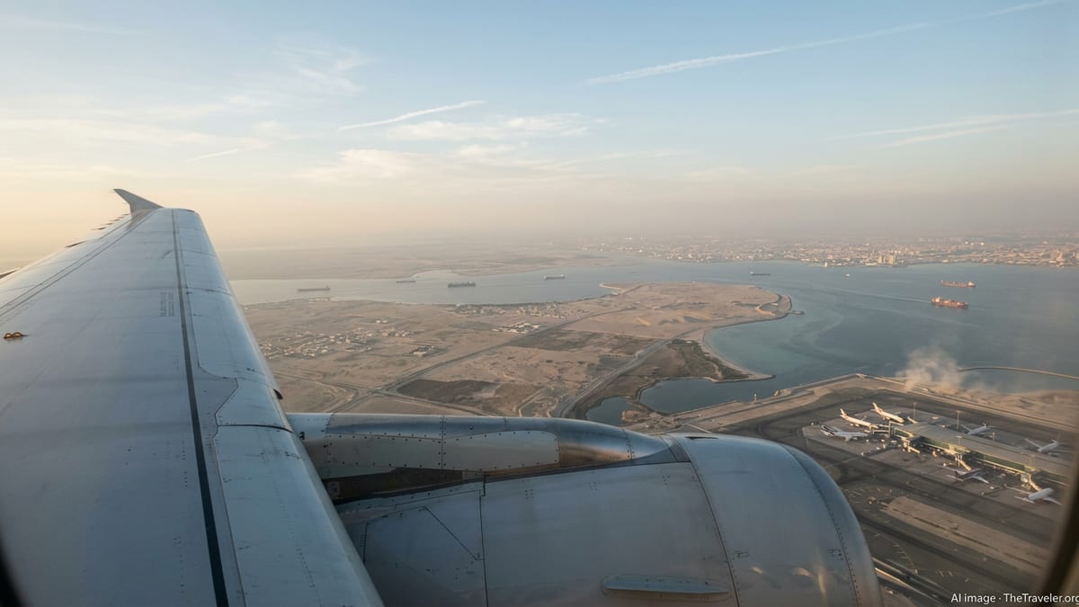 Airliner wing over a hazy Middle Eastern coastline at golden hour, with distant airport and shipping lanes below.