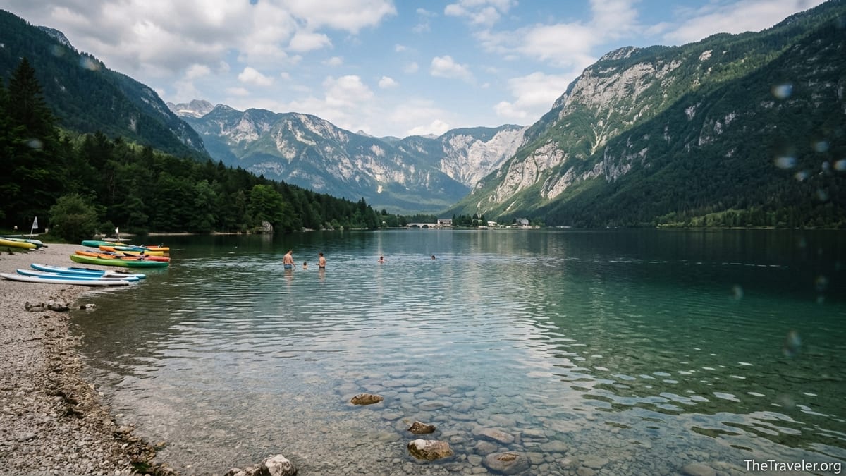 Swimmers and kayaks along the forested shore of Lake Bohinj with Julian Alps peaks behind.