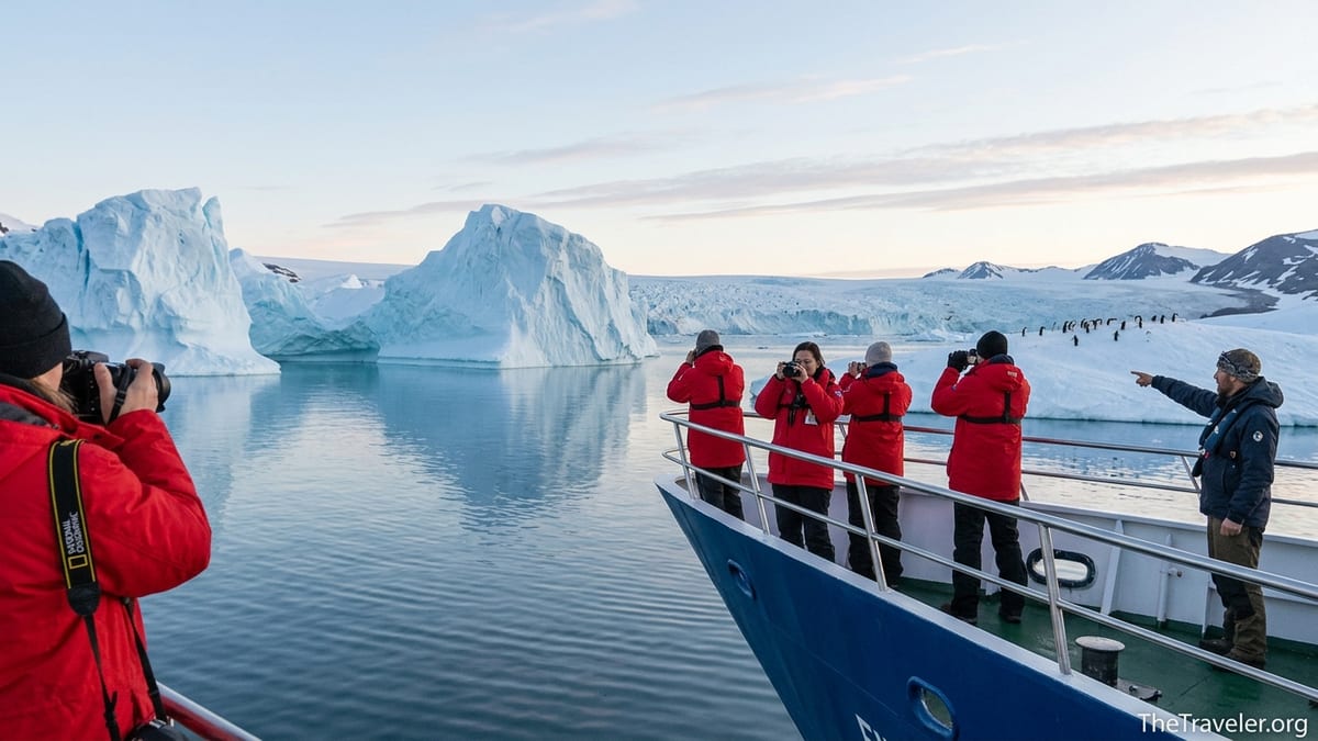 Travelers in red parkas on a small expedition ship photographing icebergs and glaciers in polar waters.