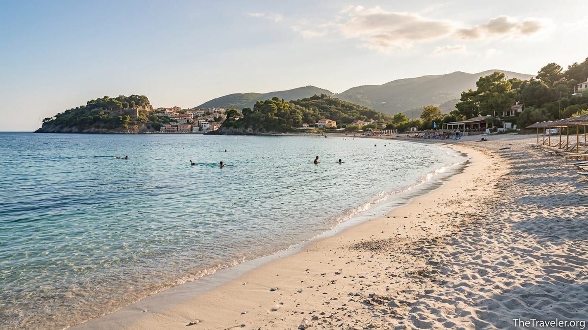 Golden hour view of a sandy mainland Greece beach curving below green hills and clear turquoise sea.