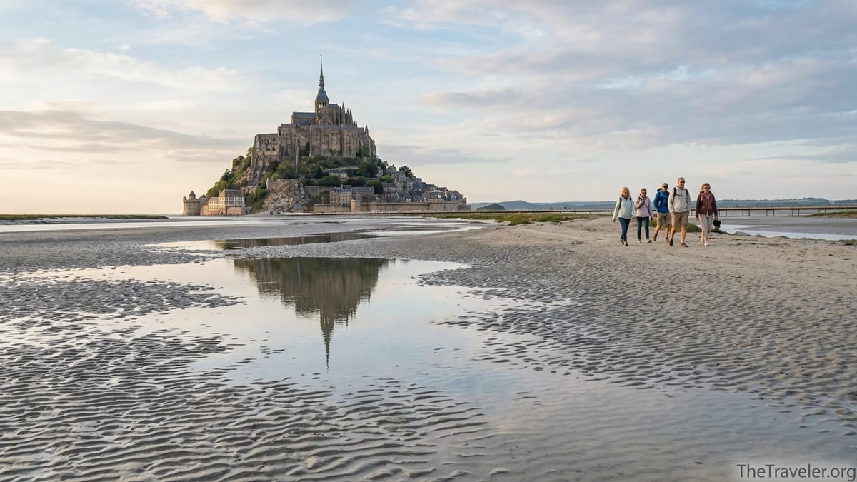 Travelers walking across tidal flats toward Mont-Saint-Michel at golden hour in northern France.