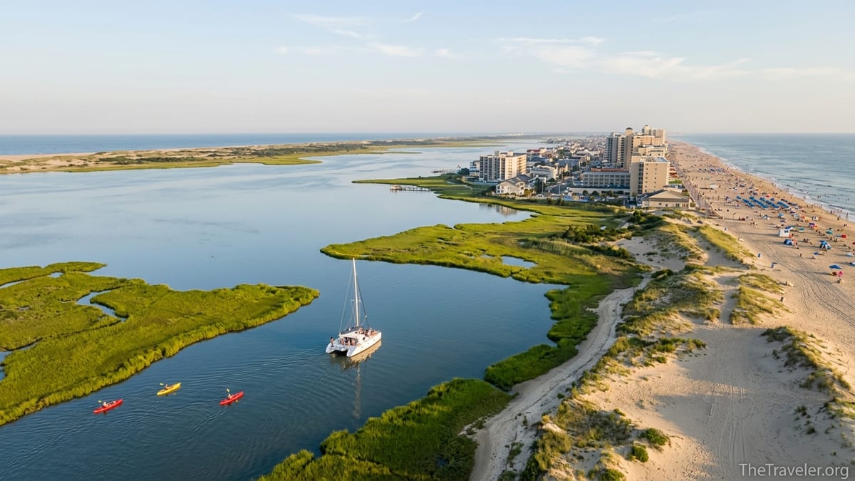 Aerial view of Ocean City, Maryland with busy beach, calm back bay, and boats near marshes at sunset.