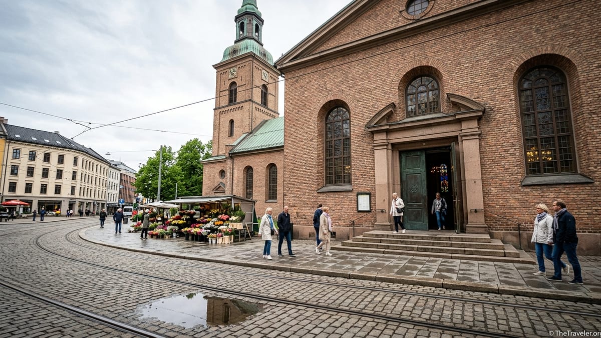 Oslo Cathedral seen from Stortorvet square with tower, portal, and people crossing the cobbled plaza.