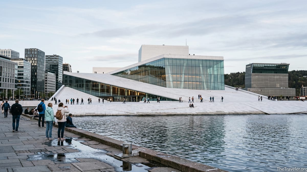 Visitors walking on the sloping marble roof of Oslo Opera House by the Bjørvika waterfront.