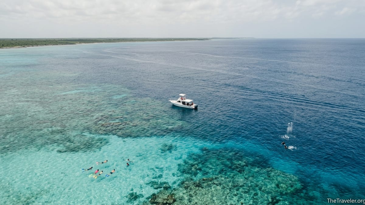A small tour boat floats over shallow turquoise reef beside deeper blue water off Cozumel’s southwest coast.