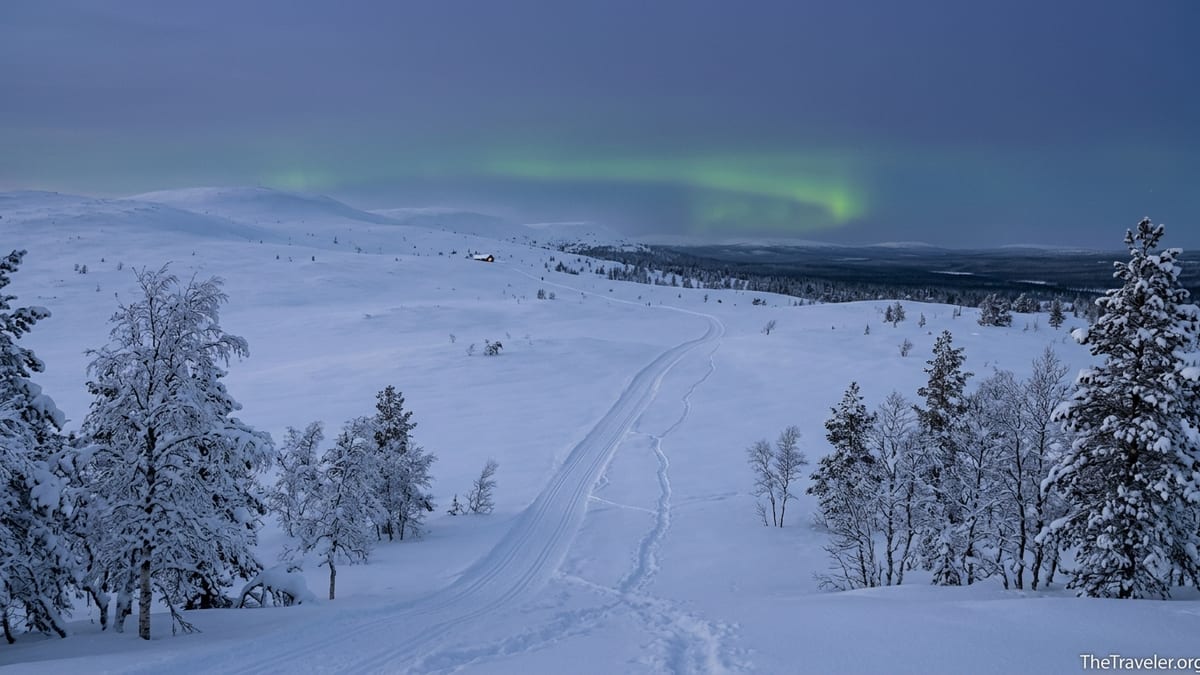 Snowy fells and ski tracks at dusk in Pallas–Yllästunturi National Park with a faint aurora overhead.