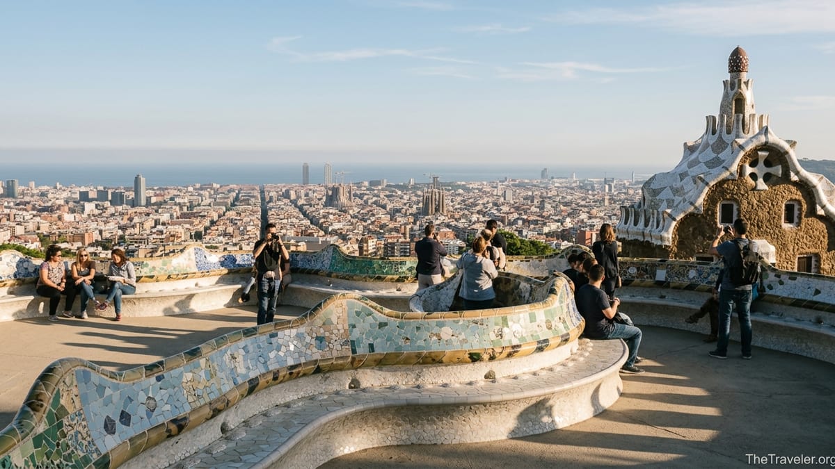 View from Park Güell terrace over Barcelona with mosaic bench, gatehouse and city skyline at golden hour.
