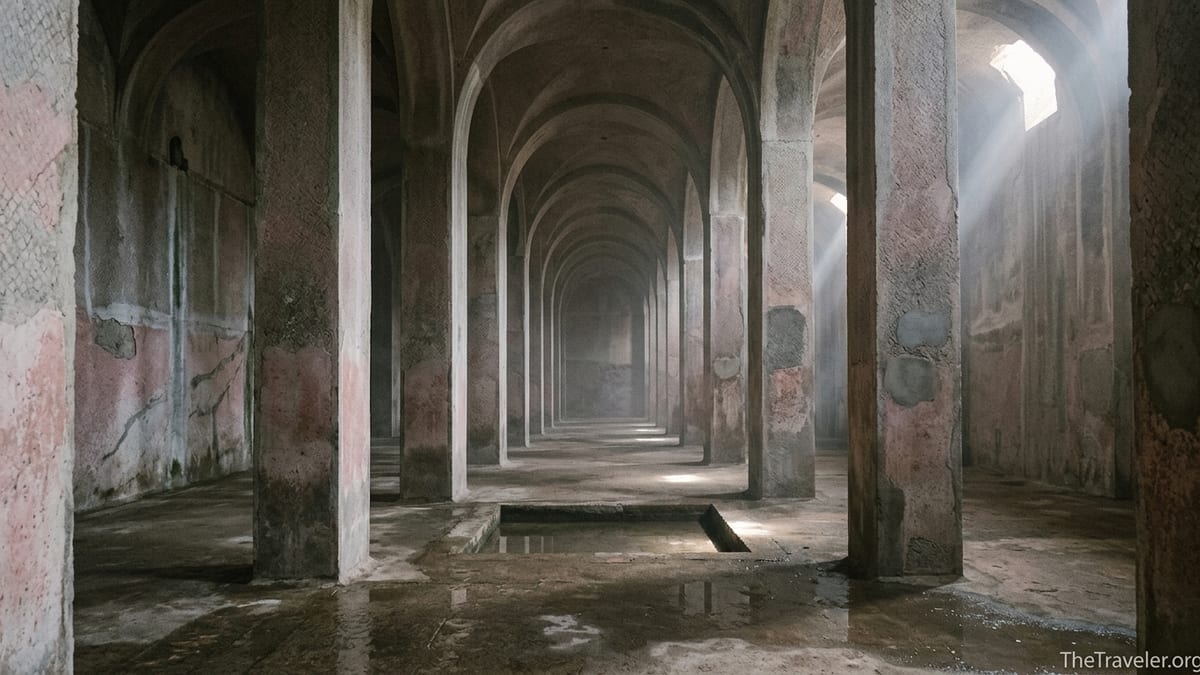Interior of Piscina Mirabilis with massive stone piers, barrel vaults and shafts of light crossing a damp floor.