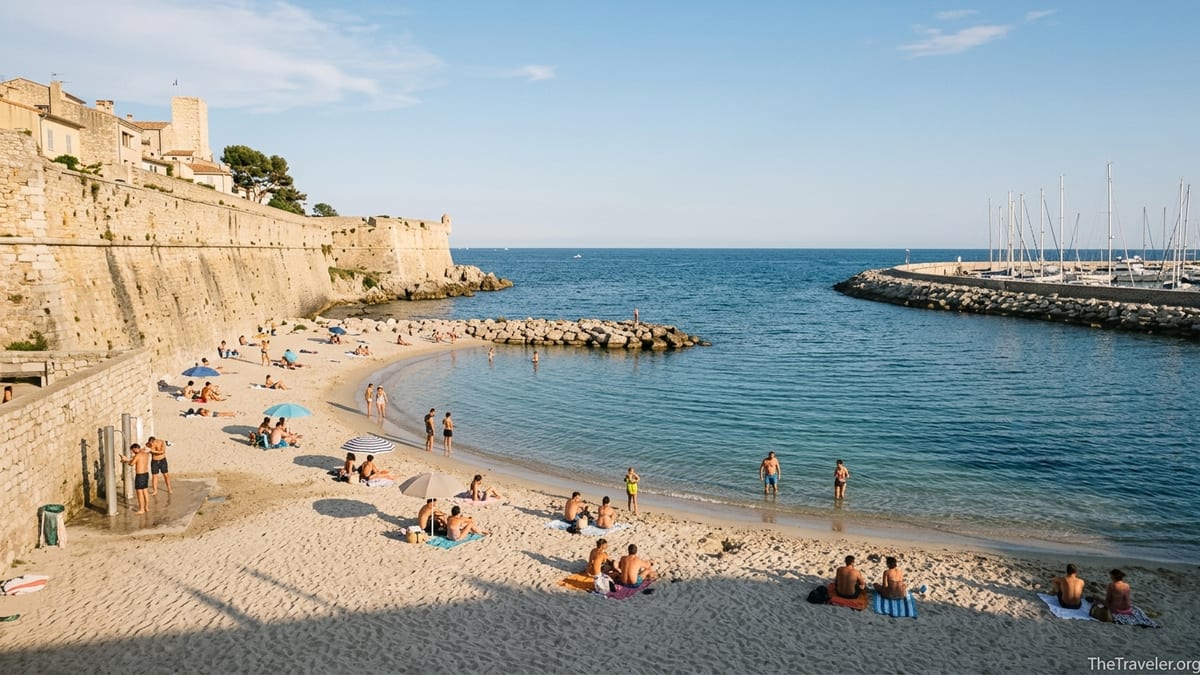 Late afternoon at Plage de la Gravette in Antibes, with sandy cove, calm turquoise water and old town ramparts.