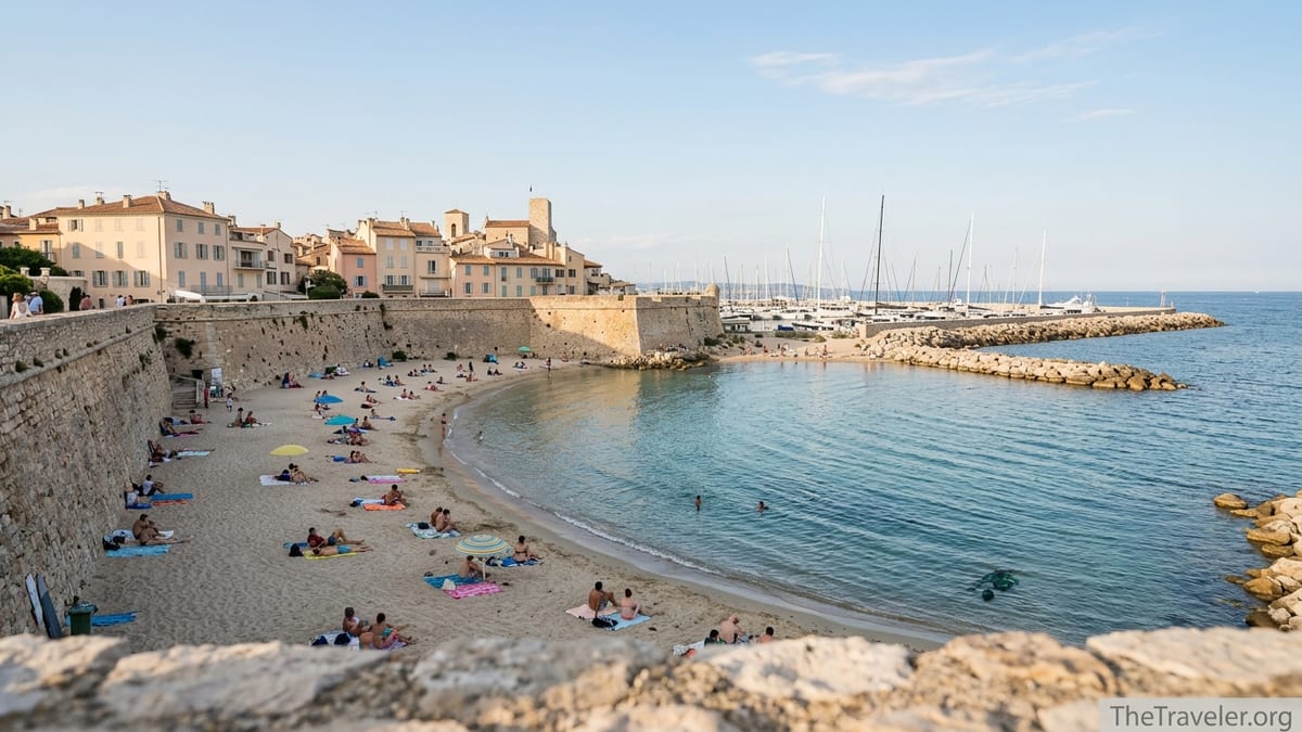 Plage de la Gravette beach in Antibes beneath stone ramparts on a calm sunny afternoon.