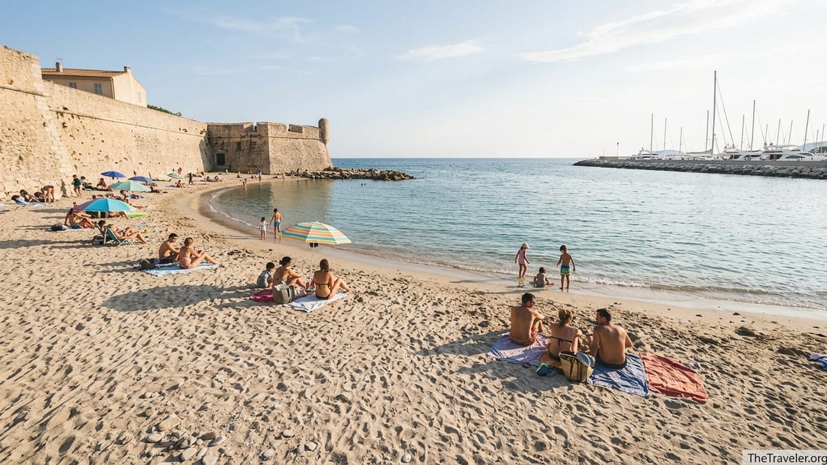 Curved sandy Plage de la Gravette below Antibes ramparts with swimmers and yachts in the background.