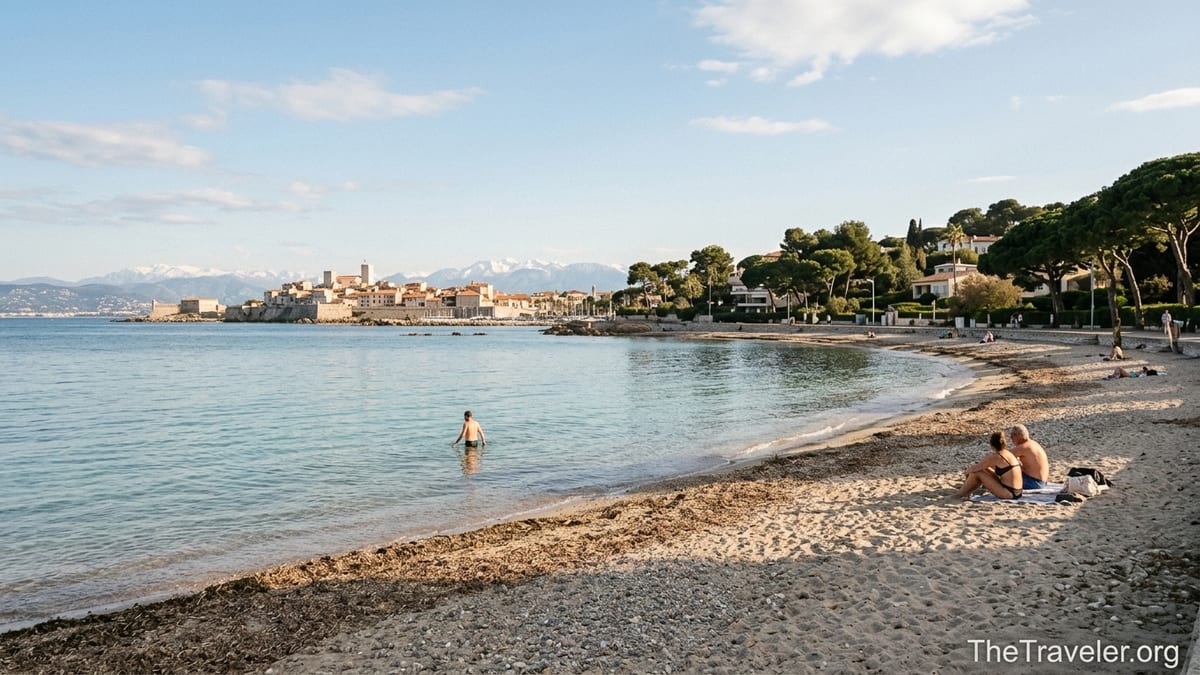 Early evening view of Plage de la Salis in Antibes with calm turquoise water, old town skyline and distant Alps.
