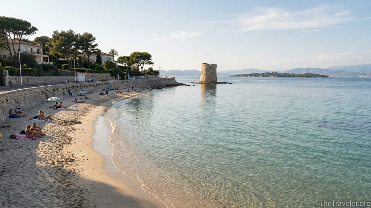 Calm sandy cove of Plage des Ondes on Cap d’Antibes with stone tower and soft afternoon light.