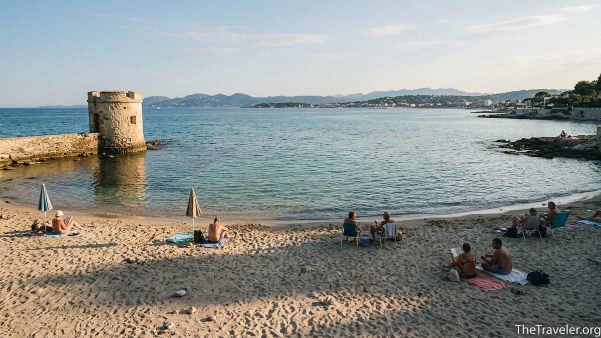 Calm late afternoon scene at Plage des Ondes, a small sandy cove on Cap d’Antibes with clear water and a stone turret.