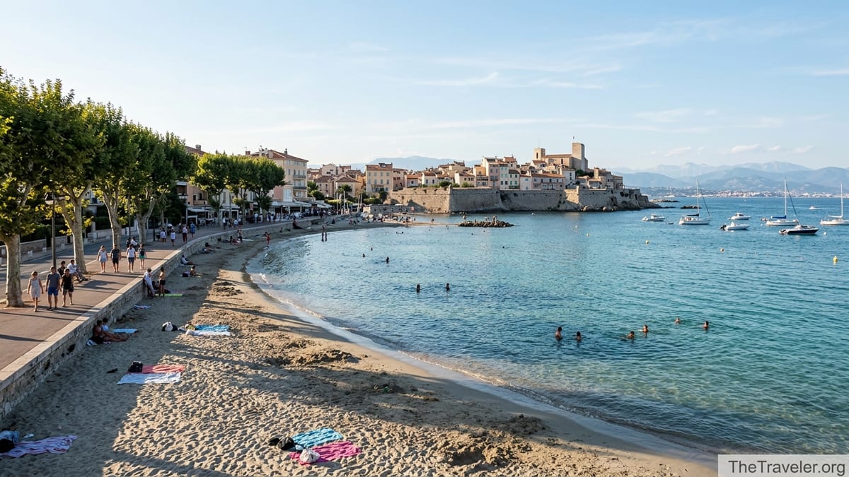 View of Plage du Ponteil in Antibes with promenade, swimmers, and distant old town ramparts on a calm sunny afternoon.