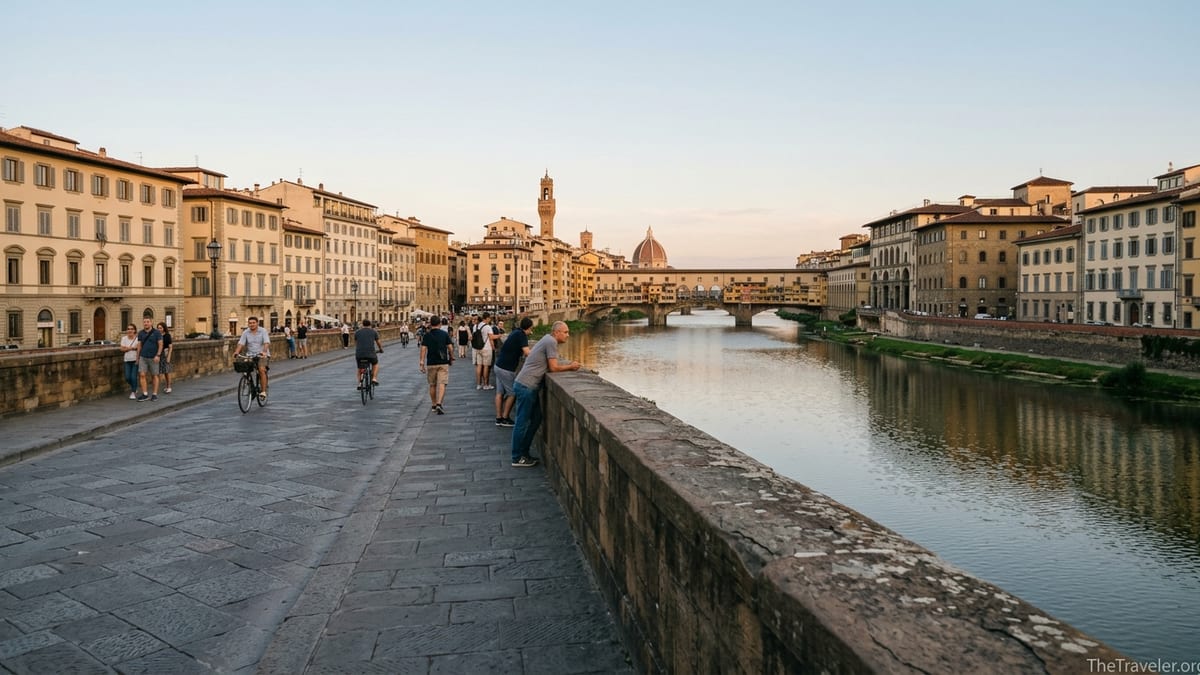 Golden hour view from Ponte alle Grazie in Florence with locals walking and the Ponte Vecchio in the distance.