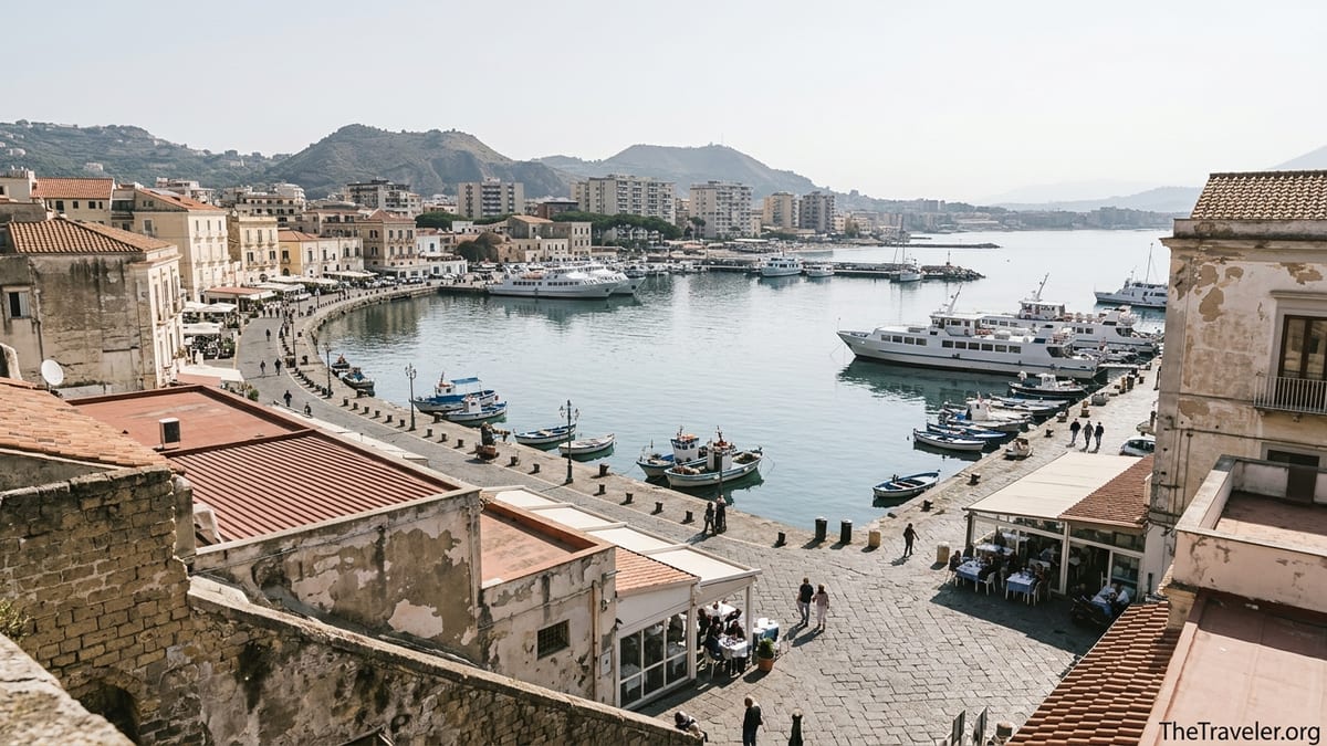 View over Pozzuoli’s harbor and historic center with ferries, seafront promenade and volcanic hills beyond.