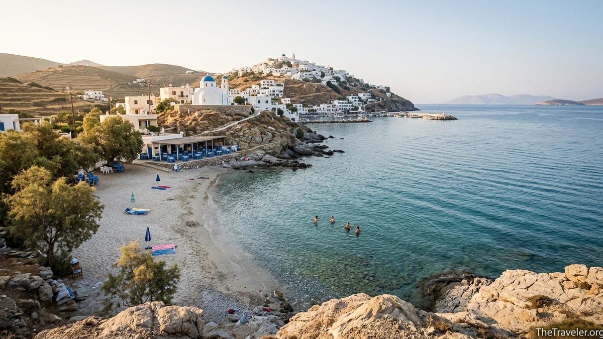 Quiet Greek island cove with few swimmers, whitewashed hilltop village and calm turquoise sea at sunrise.