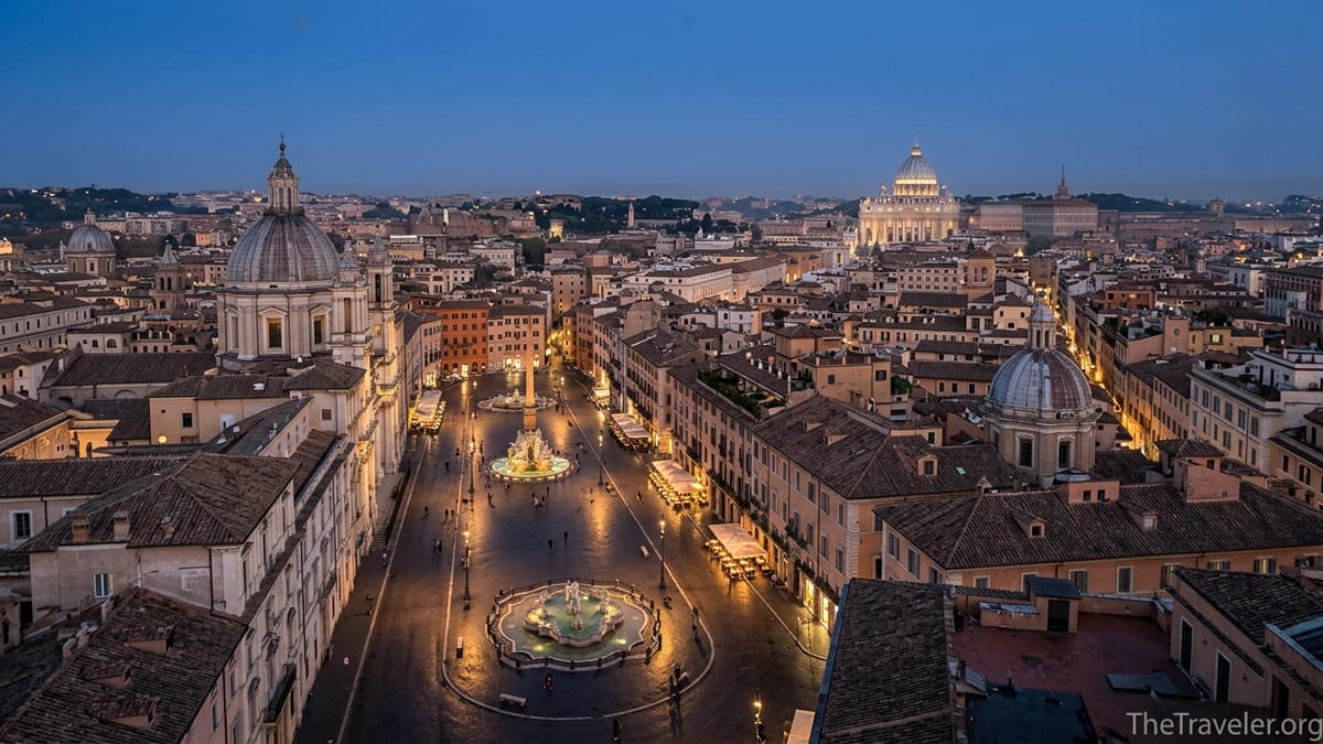 Evening rooftop view over Rome with Piazza Navona and St Peter’s dome lit against a blue hour sky.