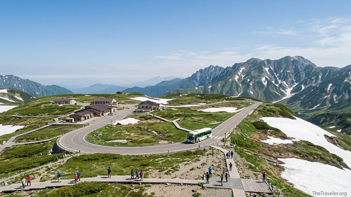 A highland bus travels across Murodo plateau on the Tateyama Kurobe Alpine Route with alpine peaks behind.