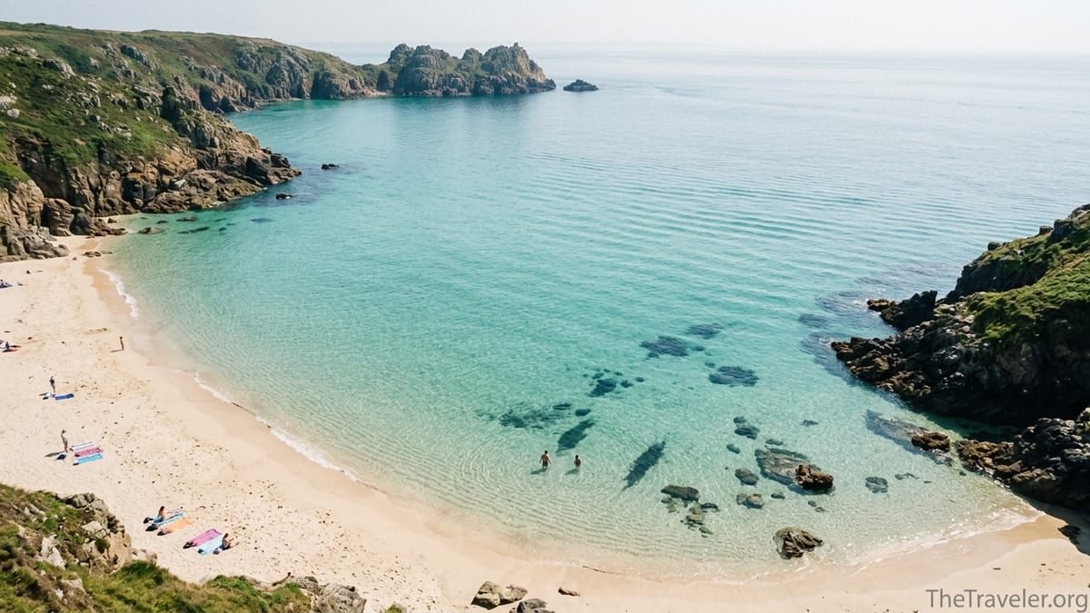 A clear turquoise cove on the UK coast with pale sand and green headlands under bright summer light.