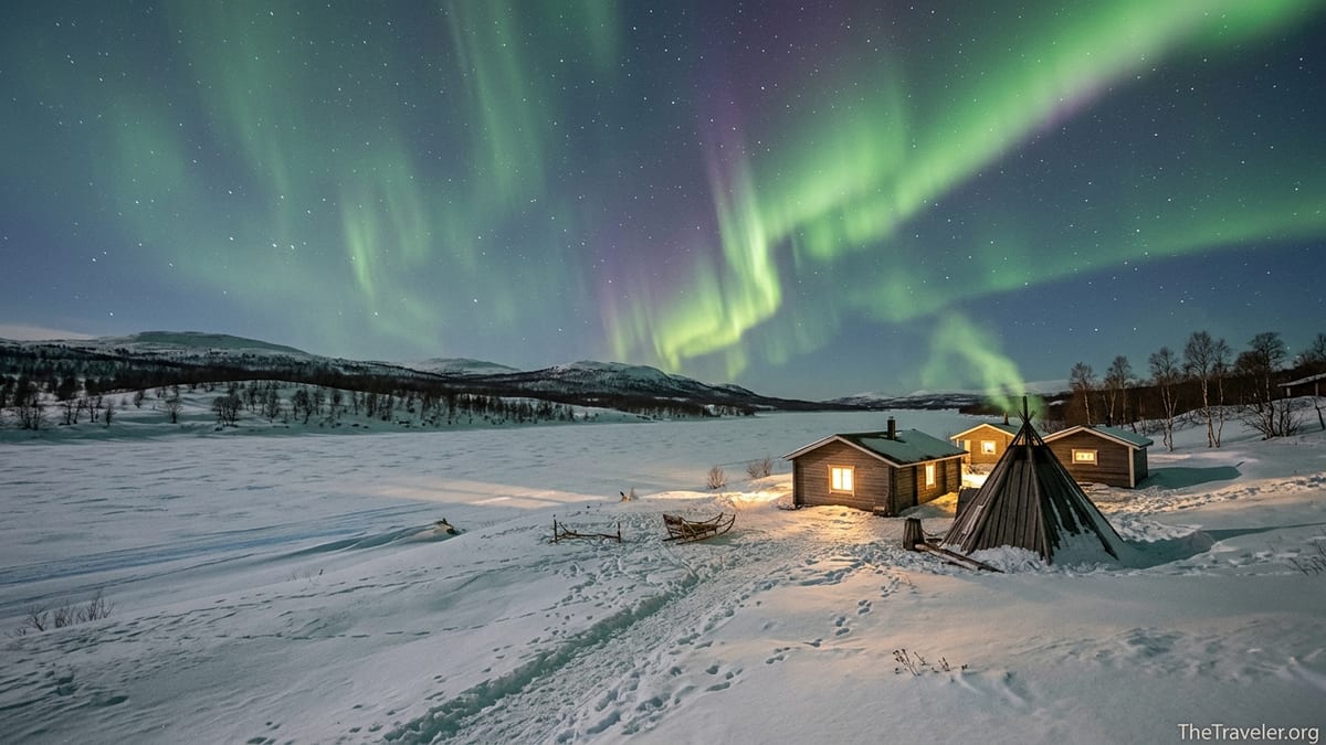 Aurora borealis over snowy cabins and frozen river near Utsjoki in Finnish Lapland at night.