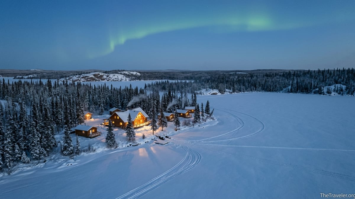 Aurora lodge on a frozen northern lake at dusk with faint northern lights overhead.